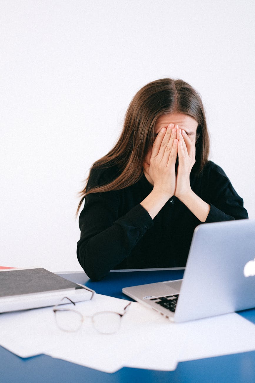 A woman seated at a computer holds her head in her hands