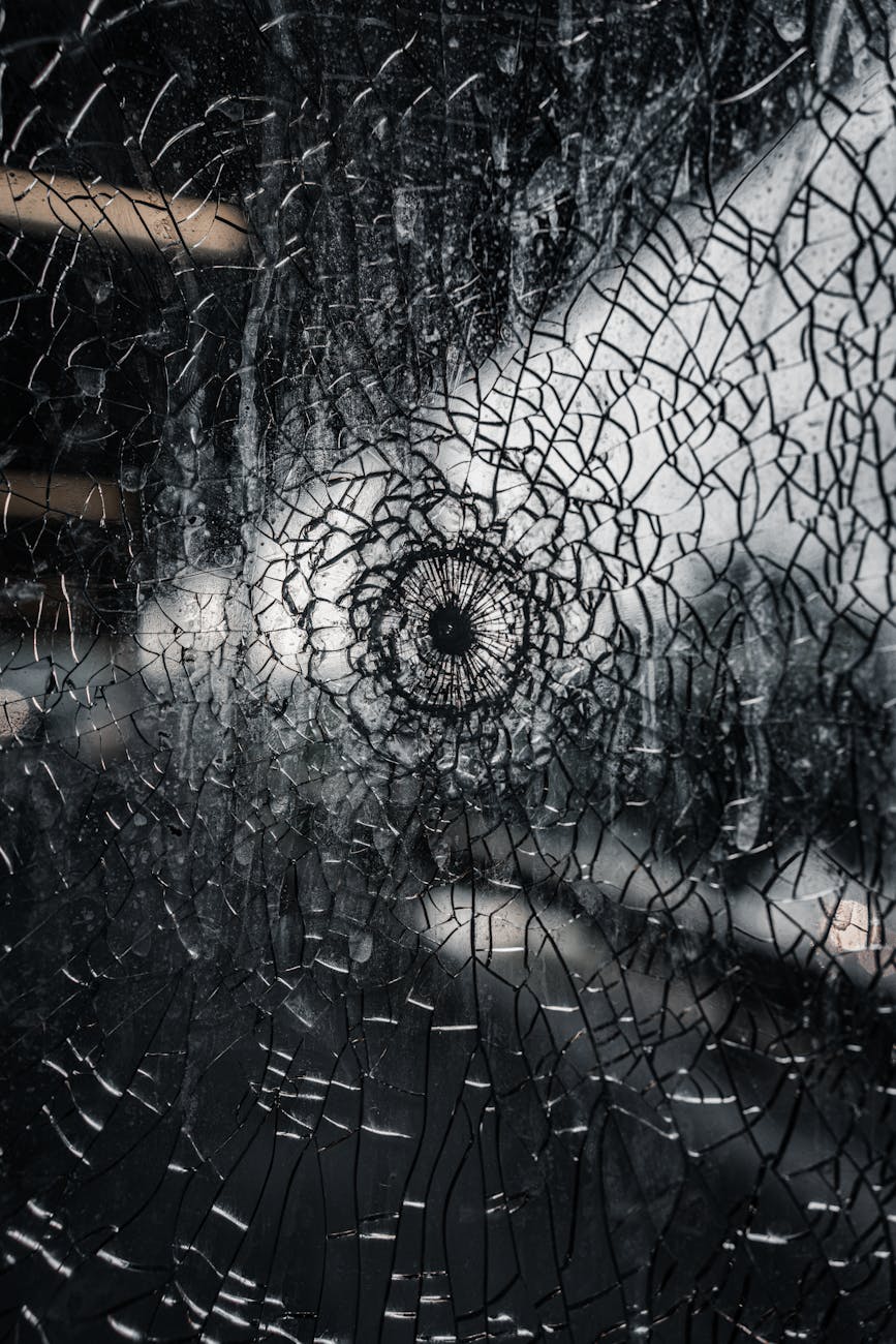 A shattered window or mirror is in the shape of a web, with the center resembling an eye, and lines of broken pieces extending out in all directions