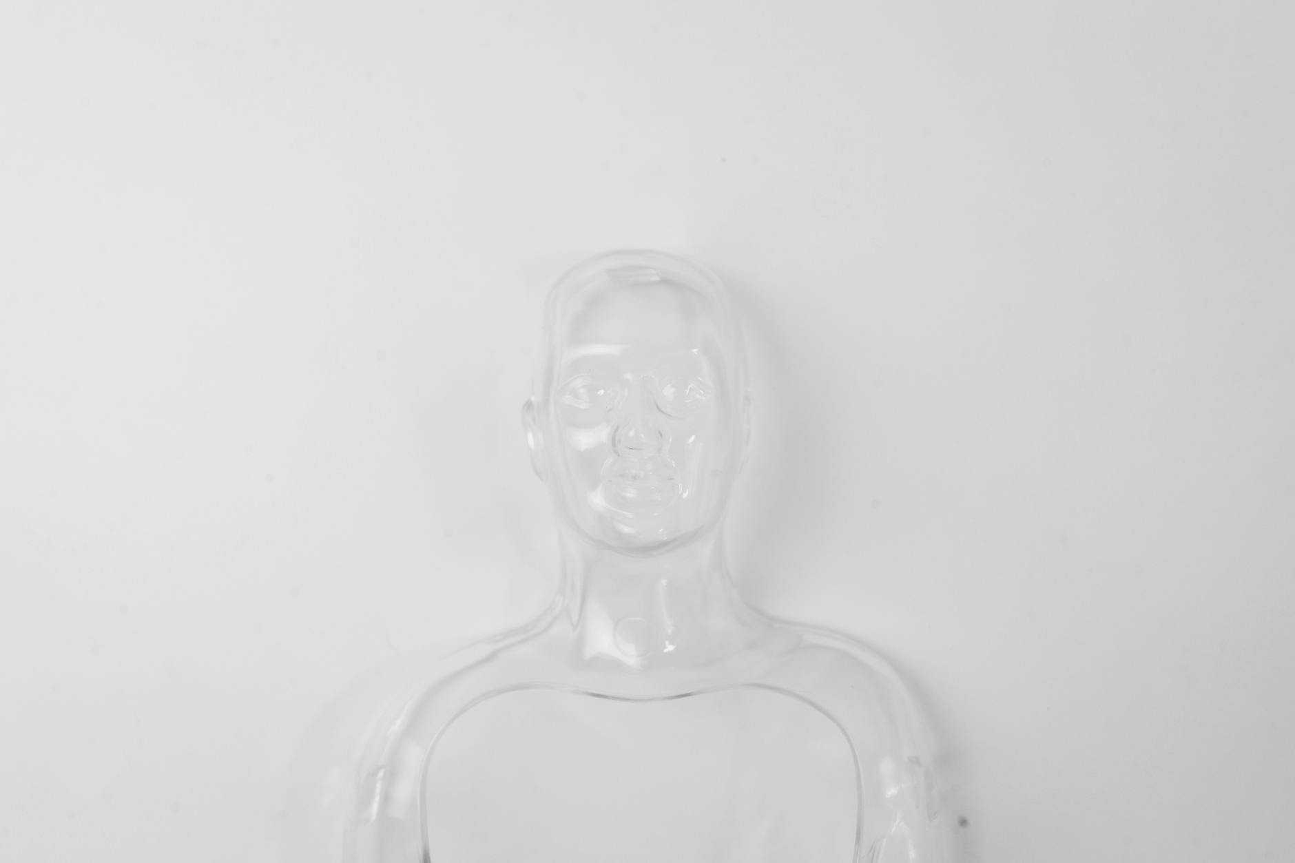 A clear empty outline of the top of a human is seen only with the shadows it makes with the light against a white wall